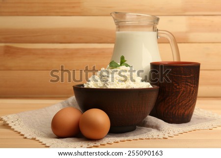 Cottage cheese in clay bowl with jug of milk and eggs on wooden planks background