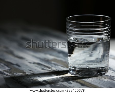 Glass of clean mineral water on old color wooden surface and dark background