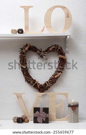 Romantic still life with wicker heart and design details on shelf and white wall background