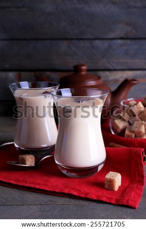 Black tea with milk in glasses and teapot with lump sugar on color wooden planks background