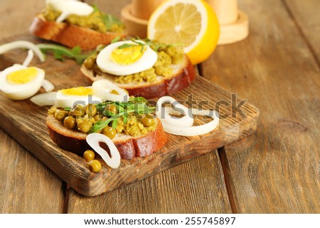 Sandwiches with green peas paste and boiled egg with onion rings and lemon on wooden planks background
