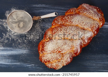 Loaf of freshly bread with strainer of flour on color wooden table background