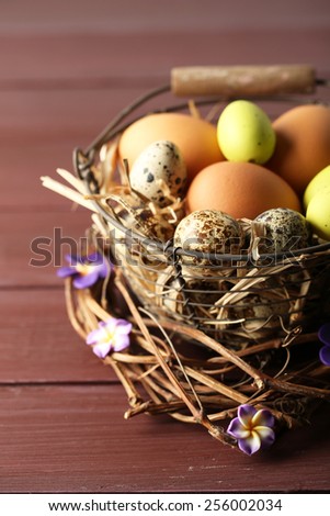 Bird eggs in wicker basket with decorative flowers on color wooden background
