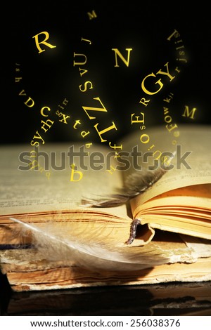 Open book with flying letters on table on dark background