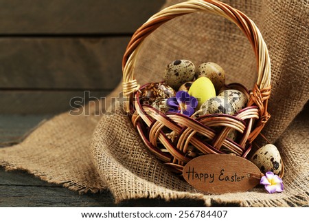 Bird eggs in wicker basket with decorative flowers on wooden background