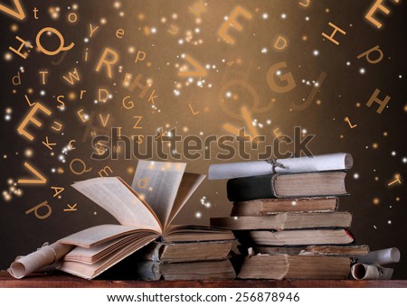 Old books with flying letters on table on dark background