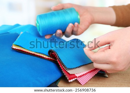 Colorful fabric samples with thread in female hands on wooden table and light blurred  background