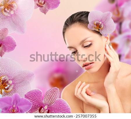 Beautiful young woman with orchid flower in hair on pink orchid flowers background