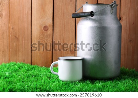 Retro can for milk and mug with milk  on green grass, on wooden background