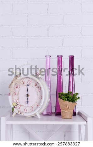 Interior design with alarm clock, plant and decorative vases on tabletop on white brick wall background