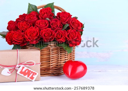 Bouquet of red roses in basket with present box on wooden background