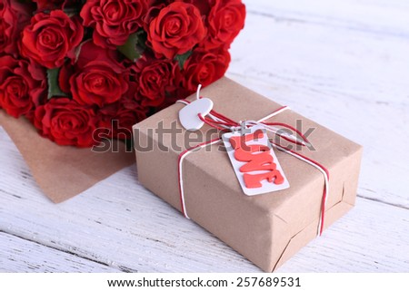 Bouquet of red roses wrapped in paper and present box on wooden background