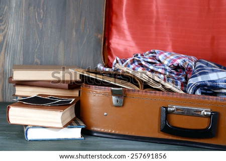 Vintage suitcase open with clothes and books on wooden background