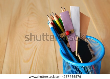 Pencils and paper notes in metal holder and wooden desk background