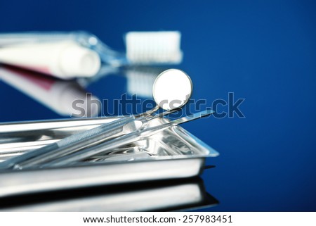 Dentist tools in metal tray with toothpaste and brush on blue background