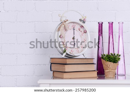 Interior design with alarm clock, plant, decorative vases and stack of books on tabletop on white brick wall background