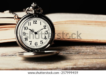 Silver pocket clock and book on wooden table