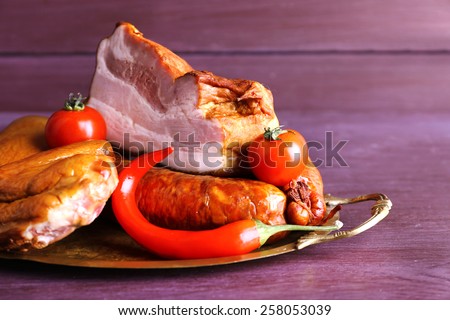 Assortment of smoked meat on metal tray on color wooden table background
