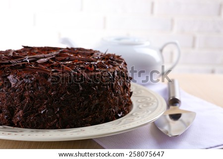 Tasty chocolate cake with teapot on table on brick wall background