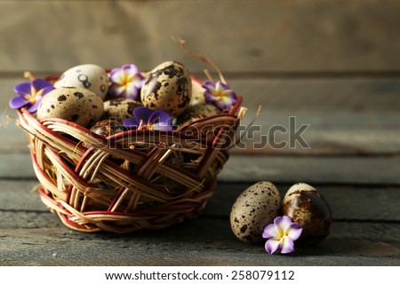 Bird eggs in wicker basket with decorative flowers on wooden background