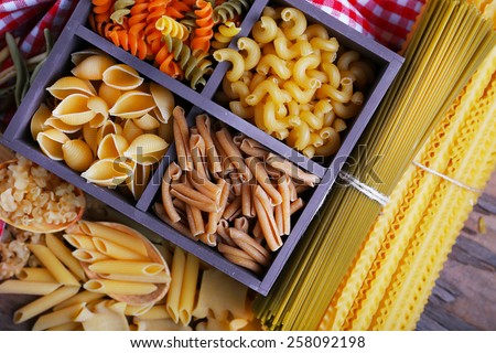 Different types of pasta in wooden box with napkin on wooden table background