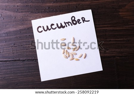 Cucumber seeds on piece of paper on wooden background
