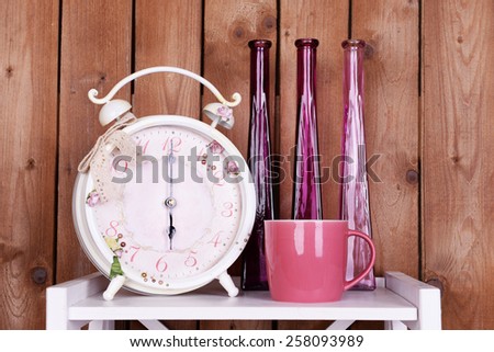 Interior design with alarm clock, cup and decorative vases on tabletop on wooden planks background