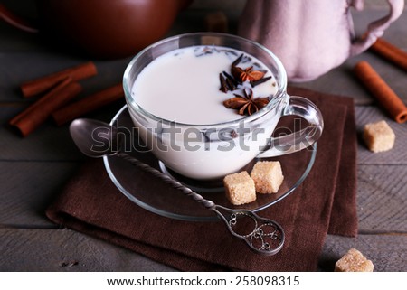 Black tea with milk in cups and teapot with lump sugar on color wooden planks background