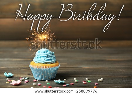 Cupcake with sparkler on table on wooden background