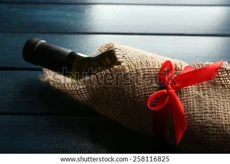 Wine bottle wrapped in burlap cloth on color wooden planks background