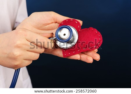 Doctor hands with heart and stethoscope on blue background