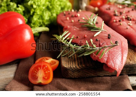 Raw beef steak with spices and greens on table close up