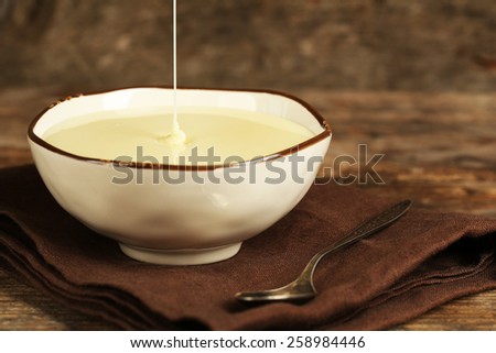 Bowl with condensed milk on napkin on wooden background