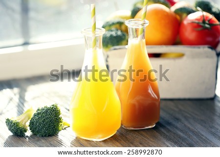 Bottles of juice with fruits and vegetables  in crate on windowsill