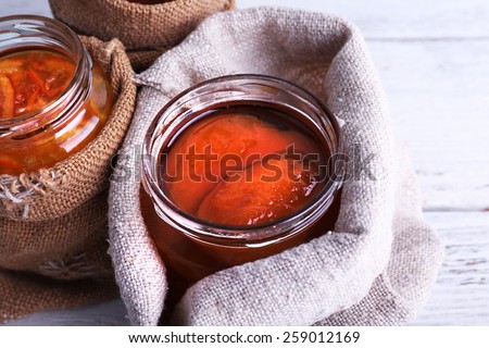 Homemade jars of fruits jam in burlap pouches on color wooden planks background