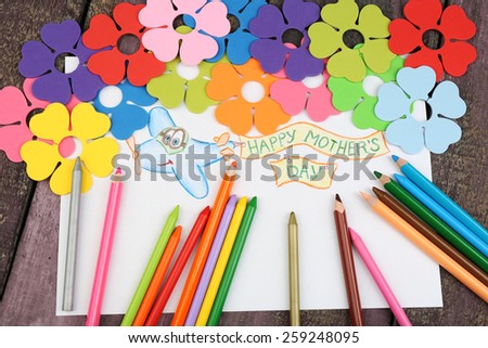 Happy Mothers Day message written on paper with pencils and decorative flowers on wooden background