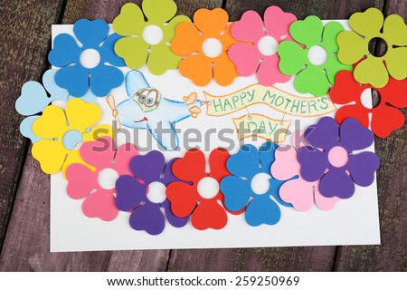 Happy Mothers Day message written on paper with decorative flowers on wooden background