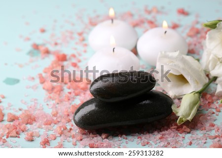 Spa stones with candles and flowers on blue background close-up