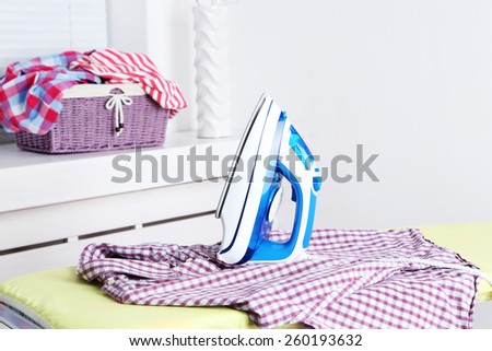 Electric iron and shirt on ironing board in room