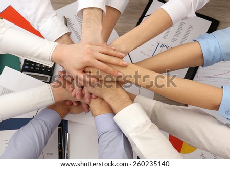 United hands of business team on workspace background, top view