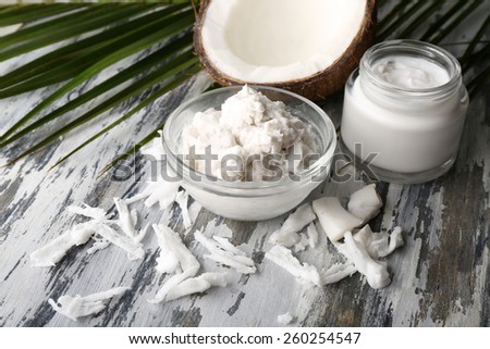 Coconut with coconut oil in bowl with jar of cosmetic cream on wooden background