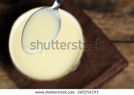 Bowl with condensed milk and spoon on table close up