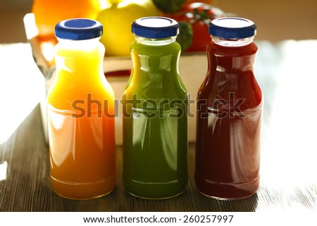 Bottles of juice with fruits and vegetables on table close up