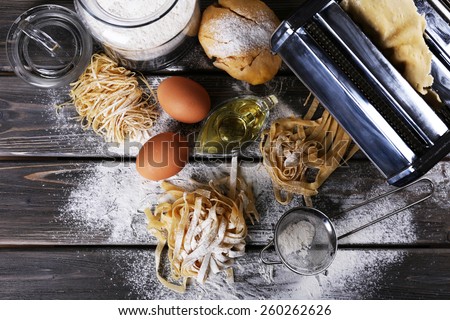 Metal pasta maker machine and ingredients for pasta on wooden background