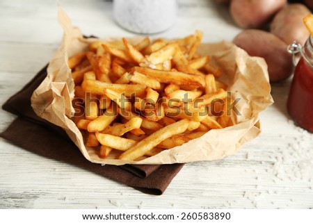 Tasty french fries on paper napkin, on wooden table background