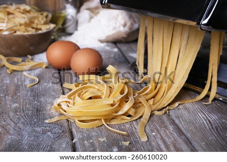 Metal pasta maker machine and ingredients for pasta on wooden background