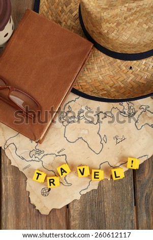 Straw hat, book and glasses with word Travel on world map and wooden planks background