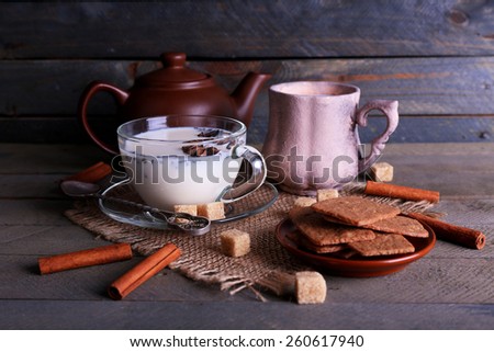 Black tea with milk in cups and teapot with lump sugar on color wooden planks background