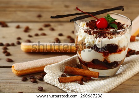 Tasty tiramisu dessert in glass, on napkin, on wooden background