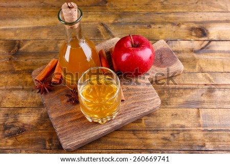 Apple cider in glass bottle with cinnamon sticks and fresh apples on cutting board, on wooden background